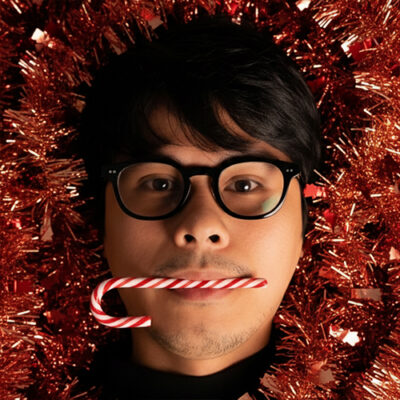 A man wearing glasses holds a candy cane, smiling cheerfully against a festive background.