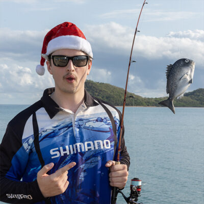 A man stands outdoors, holding a fishing pole, ready to cast his line into the water.