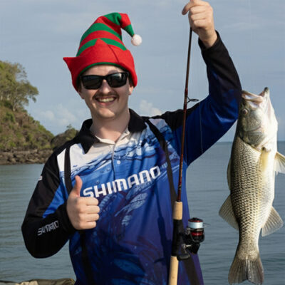 A man wearing a Christmas hat smiles while holding a large fish.
